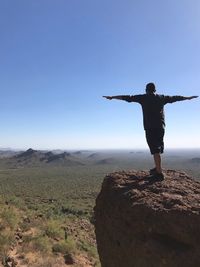 Rear view of woman standing on rock against clear blue sky