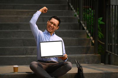 Side view of man using digital tablet while sitting on steps