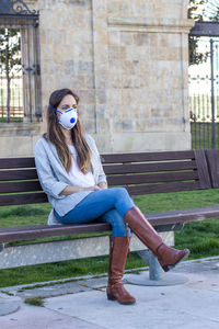 Full length of young woman sitting on bench in park