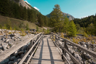 Footbridge amidst trees and mountains against sky