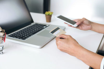 Cropped hand of woman holding credit card while using mobile phone