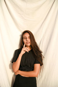 Thoughtful young woman standing against backdrop