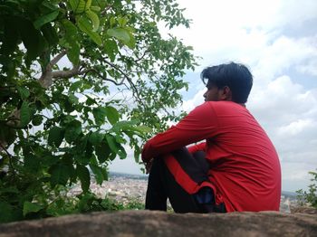 Side view of man sitting on plant against sky
