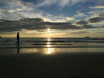 Silhouette person walking on beach against sky during sunset