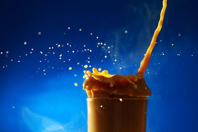 Close-up of coffee pouring in glass against blue background