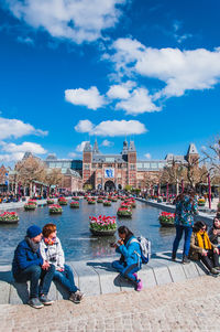 People sitting on bridge over river in city against sky