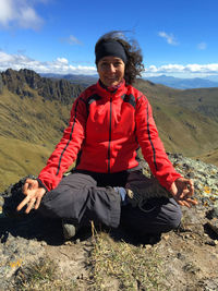 Young latin woman sitting doing yoga on a mountain top with blue sky on background