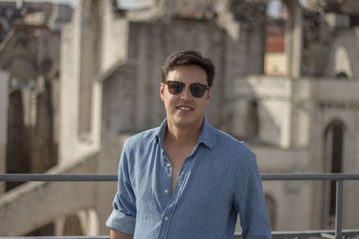 Portrait of young man wearing sunglasses standing by railing