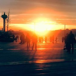 Silhouette people on street against sky during sunset