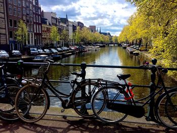 Bicycle by river in city against sky