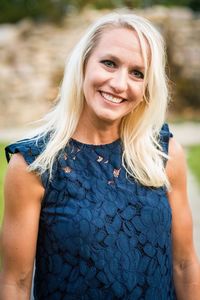 Platinum blonde smiling woman in blue dress posing for portrait in park