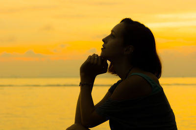 Side view of woman at beach against sky during sunset