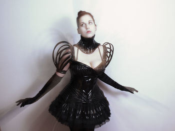 Young woman wearing costume standing against white wall