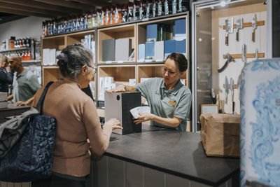 Female sales clerk giving appliance box to customer at checkout counter in electronics store