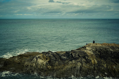 Scenic view of sea against sky with fisherman on rock formation.