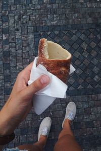 Cropped image of woman holding bread while standing on paved street