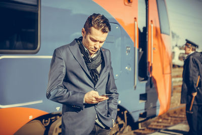 Fashionable man using mobile phone while standing against train