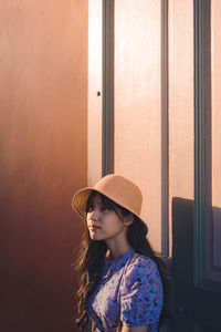 Thoughtful woman wearing hat while standing against door