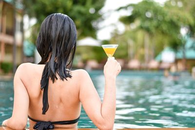 Rear view of woman holding drink while relaxing in swimming pool