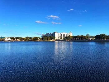 View of buildings by lake against blue sky