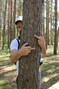 Man doing obscene gesture while embracing tree at forest