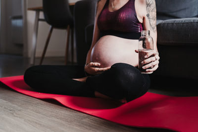 Low section of pregnant woman drinking water while sitting at home