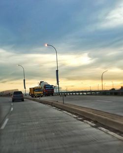 Cars on road against cloudy sky