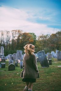 Rear view of woman standing against tombstones at cemetery