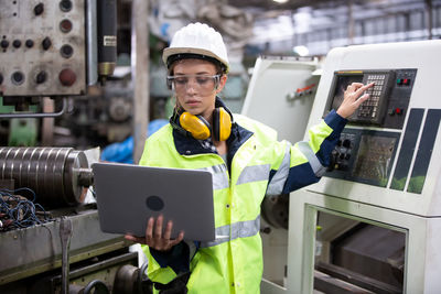 Engineer using laptop while operating machine in factory