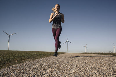 Young woman jogging on field way, wind wheels in the background