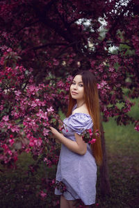 Portrait young beautiful girl teenager in a purple dress stands by a blooming pink apple tree