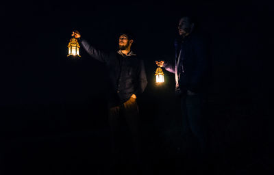 People standing by illuminated light against black background