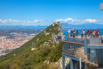 People standing at observation point by mountains against sky during sunny day