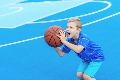 Boy aiming basketball while standing on sports court