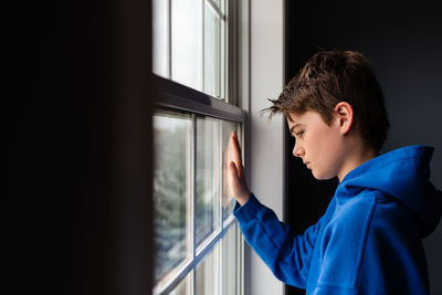 Tween boy looking out of a window in a dark room.