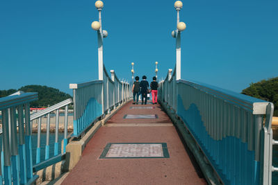 Rear view of people walking on footbridge against clear sky