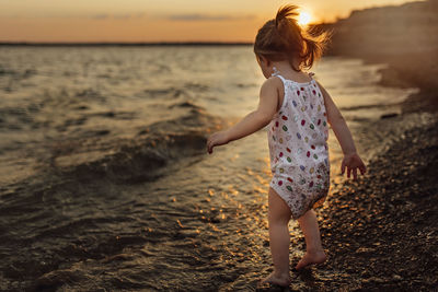 Full length of baby girl standing on shore during sunset