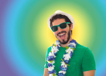 Portrait of excited man wearing sunglasses and floral garland while screaming against colored background