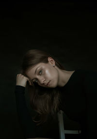 Portrait of young woman against black background