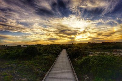 Empty boardwalk amidst landscape against cloudy sky