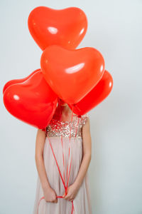 Cute girl holding balloons standing against gray background