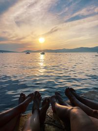 Low section of woman in sea against sky during sunset
