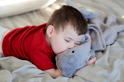 Young boy taking a nap on the bed using his plush toy as a pillow