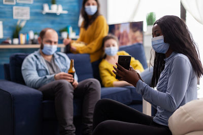 Rear view of people using mobile phone while sitting on sofa