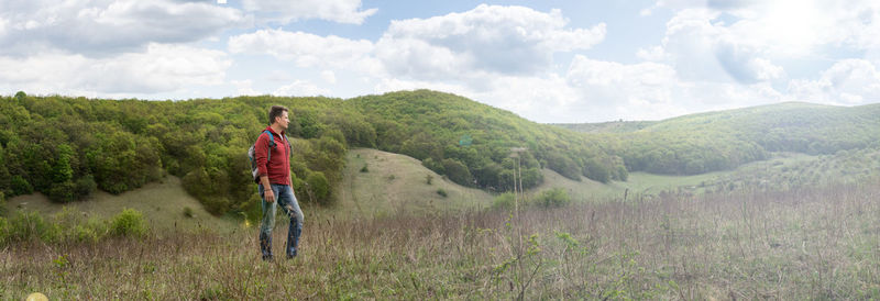 Adult man looks into the distance at the panorama of wooded hill