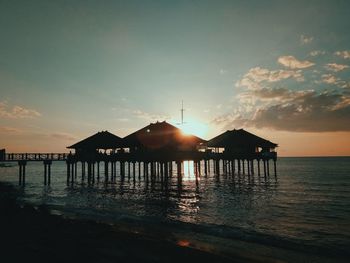 Silhouette built structure on beach against sky during sunset