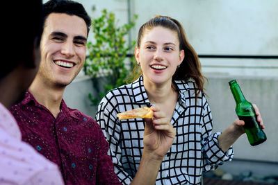 Smiling friends with food and drink talking in balcony