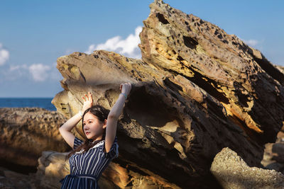 Full length of a boy standing on rock formation against sky