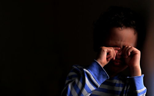 Portrait of boy covering face against black background stock photo