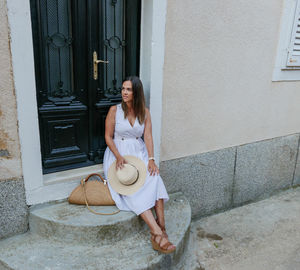 Full length of woman sitting at entrance of building